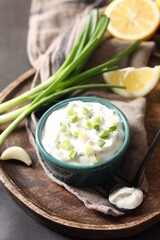 Delicious yogurt in bowl, green onion, garlic and spoon on table