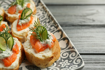 Tasty canapes with salmon, cucumber, cream cheese and dill on wooden table, closeup