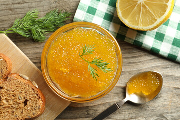 Fresh pike caviar in bowl, lemon and bread on wooden table, flat lay