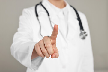 Doctor with stethoscope pointing on grey background, closeup