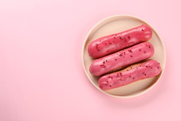 Delicious eclairs covered with glaze on pink background, top view. Space for text