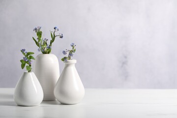 Beautiful forget-me-not flowers in vases on white marble table, closeup. Space for text