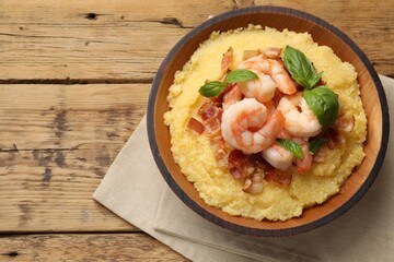 Fresh tasty shrimps, bacon, grits and basil in bowl on wooden table, top view. Space for text
