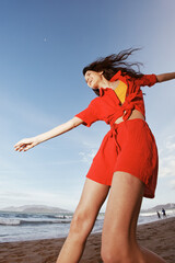 Happy Woman Dancing with Joy on a Sunny Beach: A Portrait of Freedom and Fun in Red Summer Clothes
