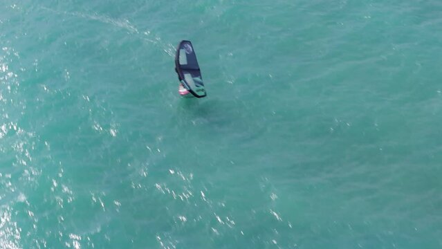 A person is seen riding a surfboard while being propelled by a parasail on the beautiful waters of Oahu, Hawaii, USA. The parasail catches the wind and helps the surfer glide smoothly over the waves.
