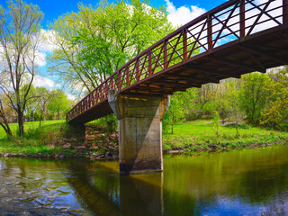 Tranquil beautiful spring forest landscape with the rustic footbridge and arching maple trees over the Big Sioux River at Parsly Park in Sioux Falls, South Dakota, USA