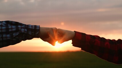 Man and woman farmer colleagues team partner hands hitting fist at sunset field bright sun closeup