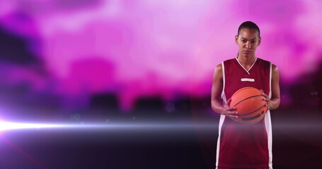 Image of african american female basketball player with ball on cloudy pink and with light beam