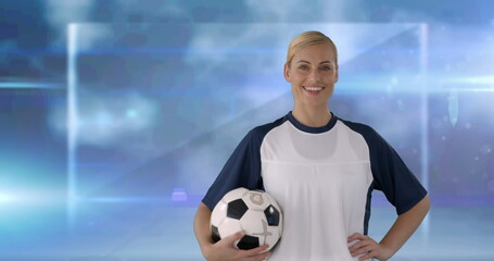 Image of happy caucasian female football player handling ball, over blurred grey with lights