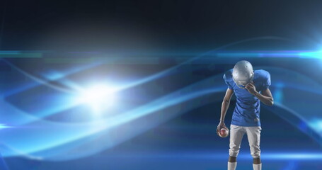 Image of excited american football player holding ball on dark background with moving lights