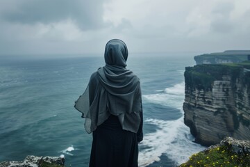 A woman stands on a cliff overlooking the ocean