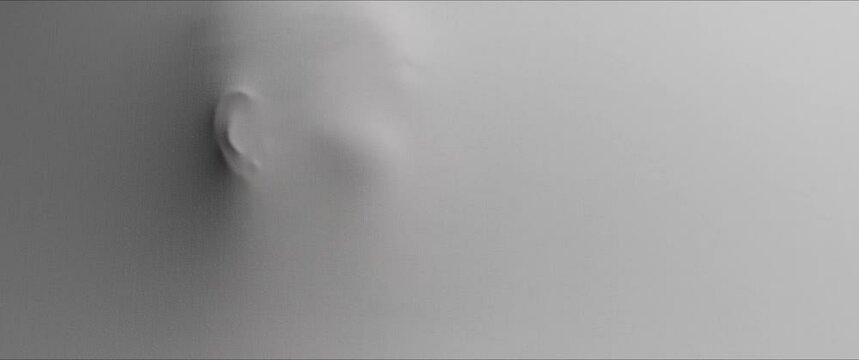 A young woman's face appears from the wall