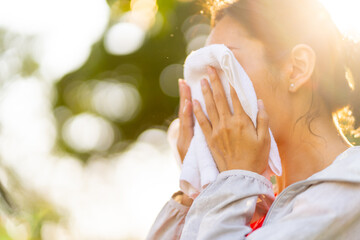 Asian woman in sportswear wiping sweat on her face with towel during jogging exercise at public...
