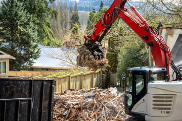 Demolition cleanup and debris removal, heavy equipment with jawbone bucket used to pickup debris and deposit in commercial dumpster for hauling away, residential construction
