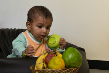 Fototapeta premium A baby trying to pick fruits. Eating, healthy, bowl, spoon, curious, happy, mother, boy, girl, toddler, kid, game, play, bib, soup, drink, sip, bite, feed, sit, cereal, beanbag, chair, health, weight