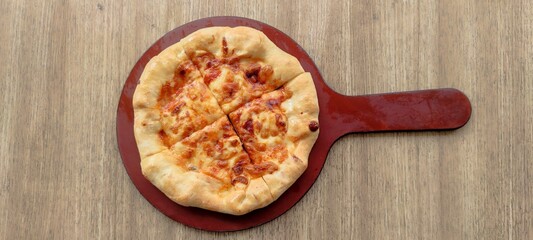 pizza served with tomato sauce and parmesan cheese served on a red pizza plate isolated on a wooden textured background
