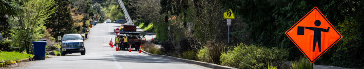 Work in progress road works orange caution sign for traffic flagger ahead, large bucket truck with...