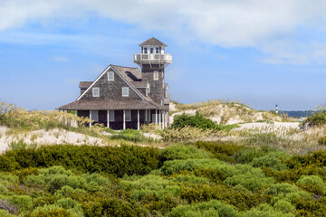 Built in 1898, historic Oregon Inlet Life-saving Station stands among the sand dunes sea oats on the North Carolina Outer Banks of Cape Hatteras with the Bodie Island Lighthouse on the horizon.