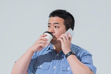 コーヒーを持ちながらスマートフォンを見る大柄な日本人男性