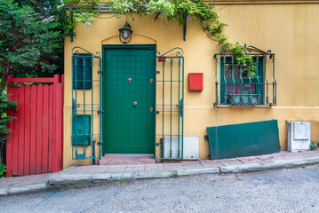 Entrance of charming yellow house with green door and windows, surrounded by climber plants and...