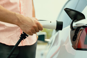 Hand insert EV charger plug into electric vehicle to recharge EV car battery from outdoor charging...