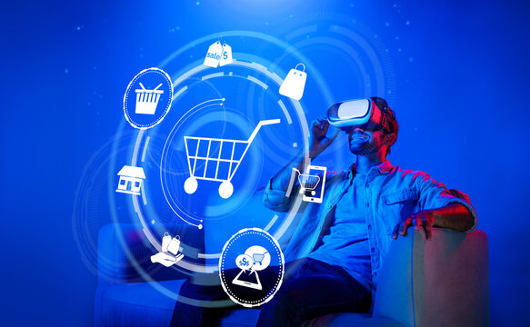 Happy man using VR headset and shopping online while sitting at sofa with shopping bags. Smart person looking at online market hologram and icon with neon background. Innovation technology. Deviation.