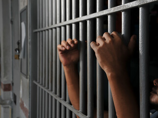 hands of a prisoner behind prison bars	
