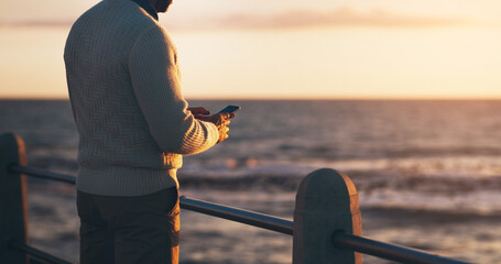 Man, phone and texting on promenade by ocean with sunset sky on vacation with contact on web....