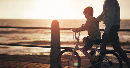 Father, boy and bike for teaching at beach, promenade and sunset on vacation with care, love and...
