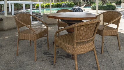 The recreation area by the swimming pool. Wicker plastic chairs stand at a round table. Ornaments on the concrete floor. Green vegetation in the distance. Philippines. Cebu.