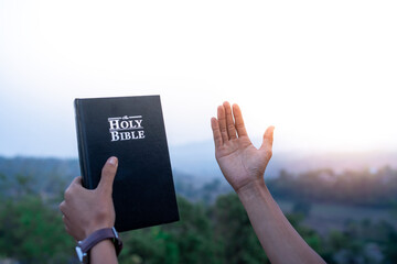 person raised both hands up and holding bible pray for blessings to God.