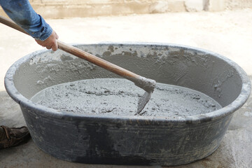 Close up worker using a hoe to mix cement powder, sand, stones in basin for mixing cement. Concept....