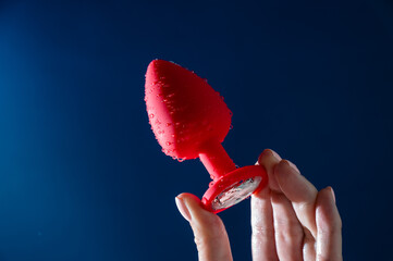 Woman holding red anal plug in water drops on blue background. 