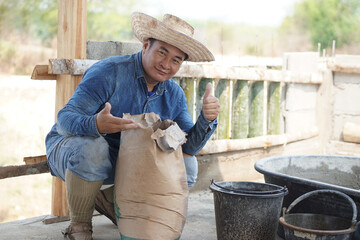 Handsome Asian man worker is at construction site, sits beside bag of cement powder, thumbs up....