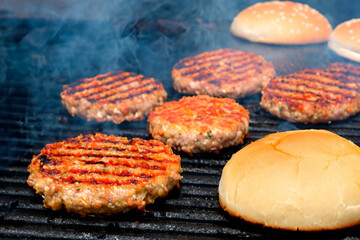 Ground beef burger patties and burger buns grilled on a barbecue grill