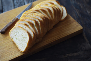 long loaf on a wooden board and knife isolated on a white background. Tasty bread