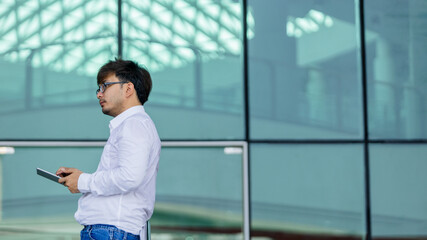 A man wearing a white shirt and glasses is holding a tablet in his hand