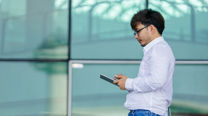 A man wearing a white shirt and glasses is holding a tablet in his hand