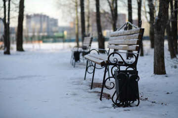 park bench on a winter alley at snowfall. bench with snow after snowstorm or in snow calamity in...