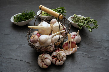 Fresh garlic bulbs and garlic cloves in a small old metal basket and fresh green herbs in porcelain...