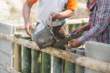 Close up workers help each other to pour cement into bamboo molding for building at construction...