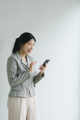 Young woman in business attire reacts joyfully to smartphone message in bright office environment.