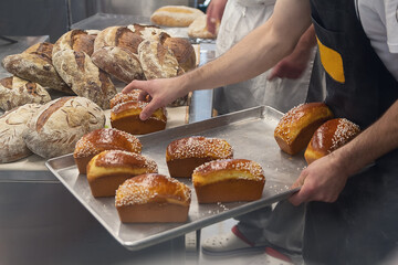 Baker in a bakery places fresh bread on a tray