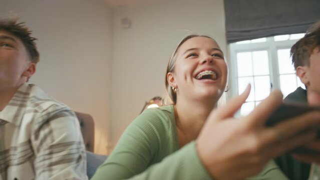 Close up of group of teenage girls and boys at home hanging out laughing gaming on mobile phones in bedroom together  - shot in slow motion
