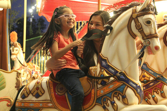 Divorced single mom and 5 year old brunette Latina daughter spend fun time on amusement park carousel