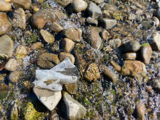 Plastic waste lies on rock of a riverbed background. Environmental issues. Stock photo.