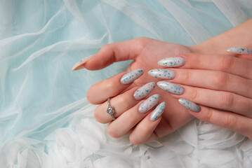 Female hands with blue nail design on blue silk background.