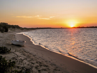 A Golden Sunset with a small rowboat moored on the sandy beach next to a secluded bay in Portugeuse...