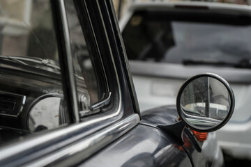 side rear rear view mirror of a classic vintage retro car. Old black vehicle with chrome details; vintage round side view mirror and window
