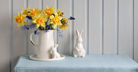 bouquet of yellow daffodils and blue hyacinths in a white jug on the table, Easter bunny, festive...
